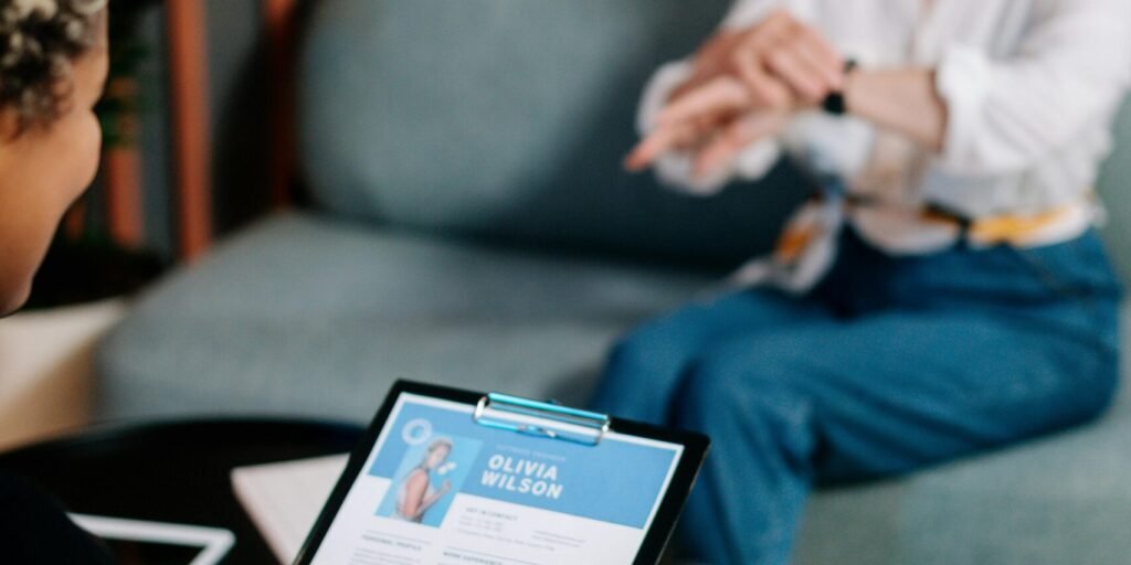 A senior woman being interviewed indoors with her resume displayed.