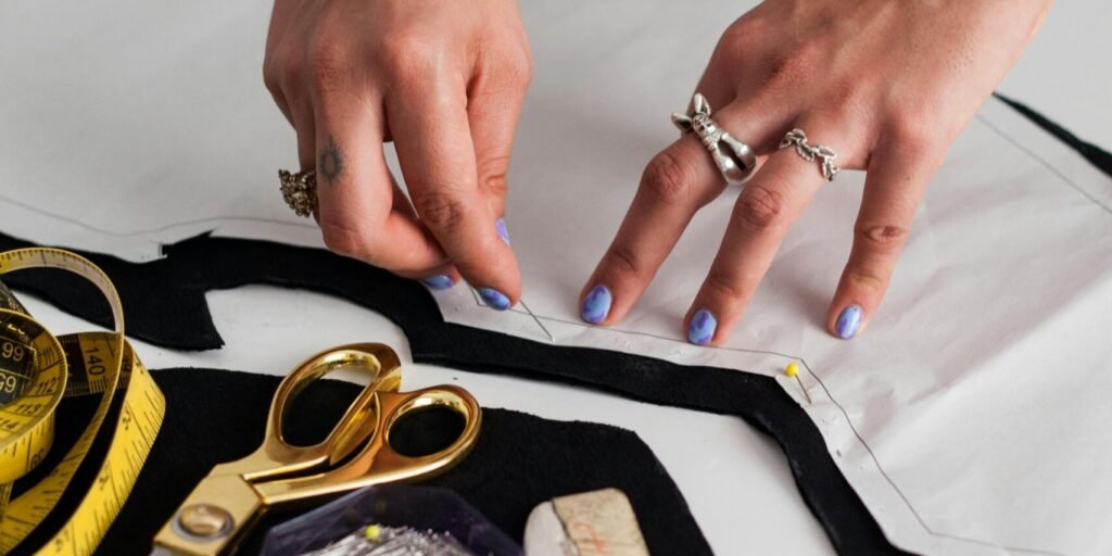 Hands working on fabric with sewing tools in a fashion designer's workspace.